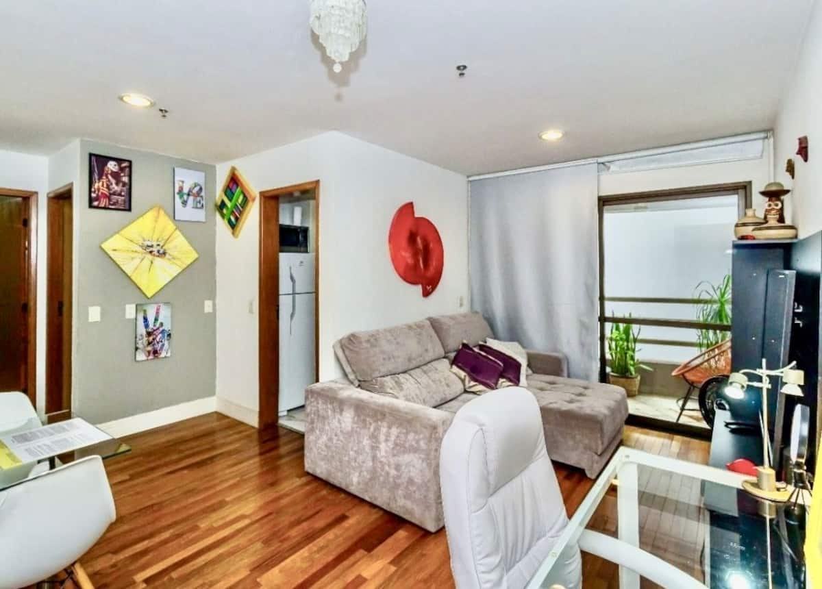 Sala de estar do Cozy Ap, com sofá, mesa de jantar e piso de madeira